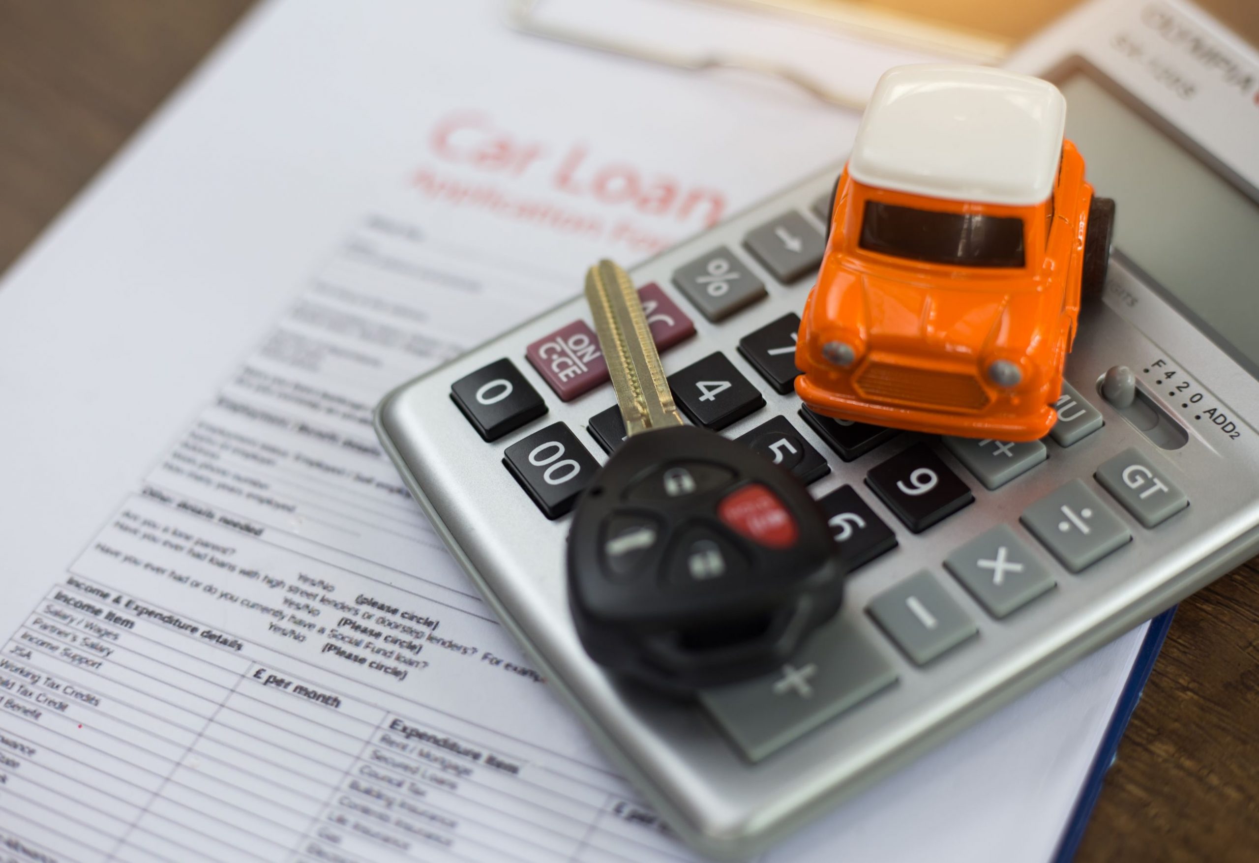 Toy car and car keys on top of calculator and finance agreement