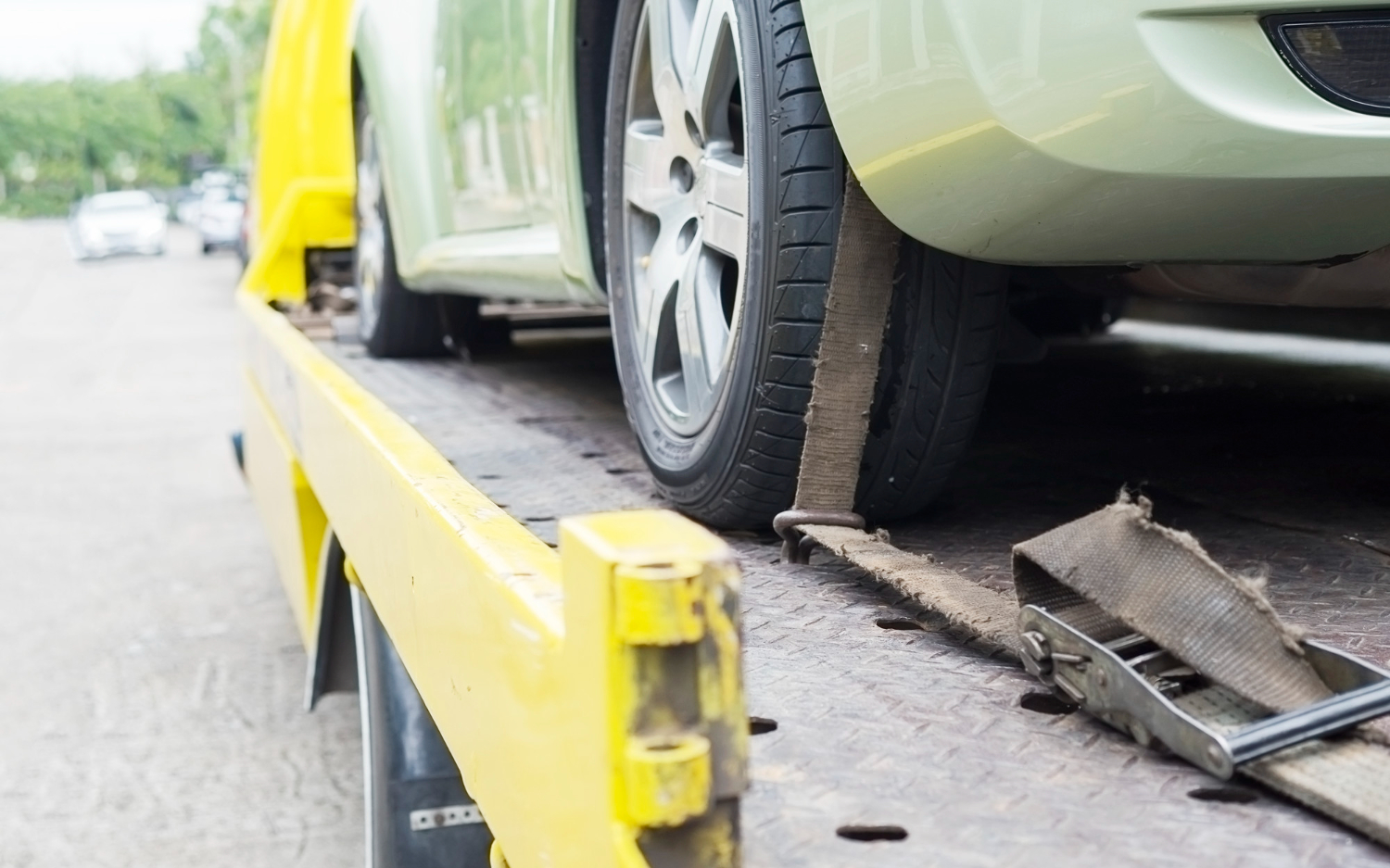A clamped green car being towed on a truck.