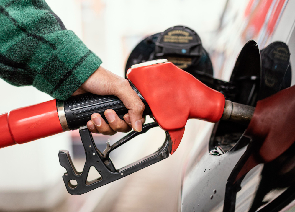 Hand holding a red nozzle filling car with fuel.
