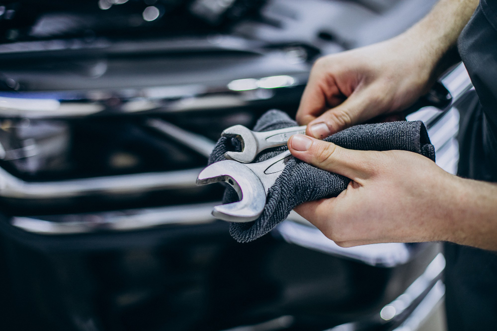 Two hands wiping down repair tools with a cloth in front of a car's engine.